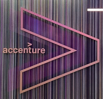 A dotted pink Accenture chevron and wordmark on a chainmail curtain, beside a reception counter marked ‘Z’.