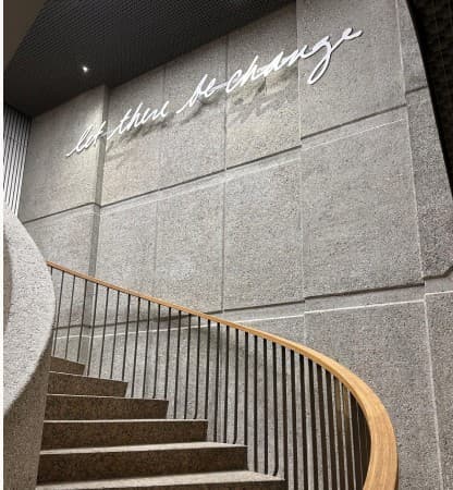 The words ‘let there be change’ in script lighting above a curved staircase.