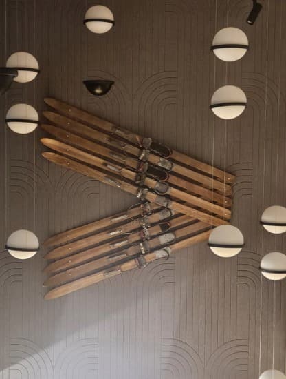 A pair of vintage wooden skis mounted on a ribbed wall between rows of spherical pendant lights.