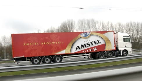 An Amstel-branded articulated lorry in red livery, travelling on a motorway.