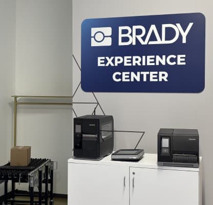 A Brady Experience Center wall sign above a bench of label printers.