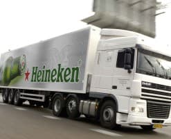 A Heineken-branded semi truck traveling on a highway, motion blur in the road behind it.