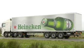 A Heineken-branded trailer in the green bottle livery, parked on grass beside a road.