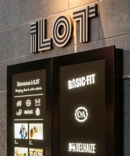 An illuminated ILOT wayfinding totem listing the center's retailers.