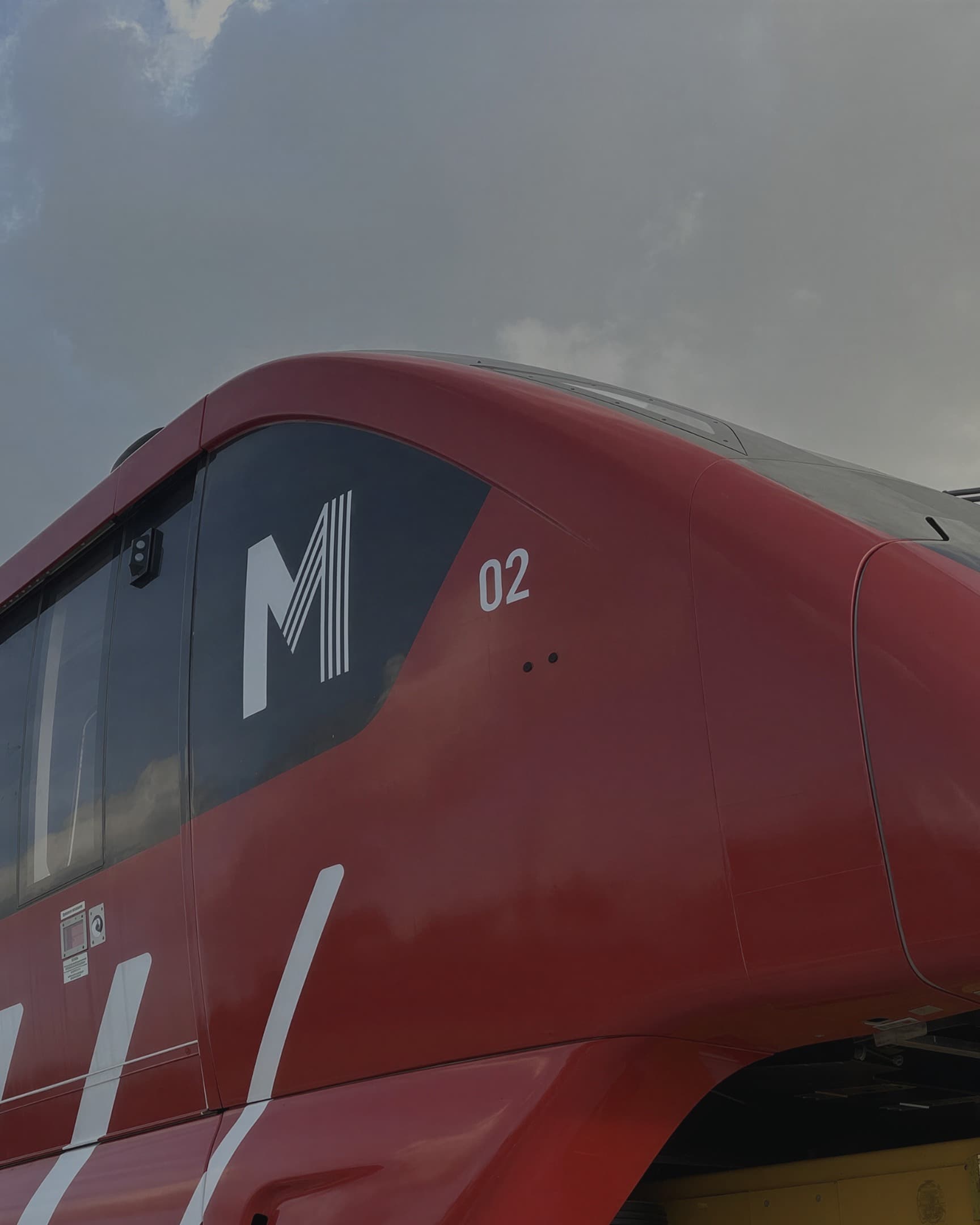 The nose of a newly branded Alstom metro car standing on the platform at dusk, its red livery and white graphics applied.