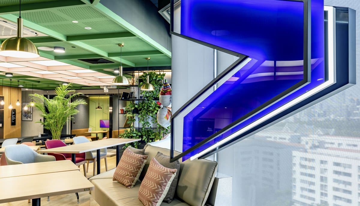 A blue illuminated Accenture chevron above a lounge area, the city beyond the glass.