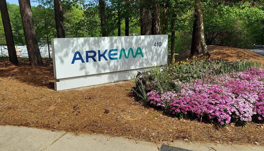 A low Arkema monument sign set among flowering planting at a site entrance.