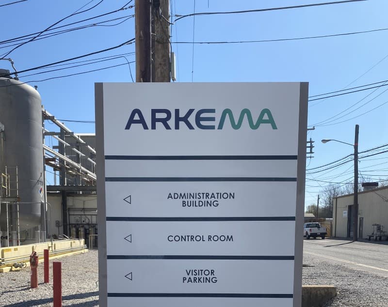 An Arkema site directional sign for the administration building, control room and visitor parking, an industrial facility behind it.