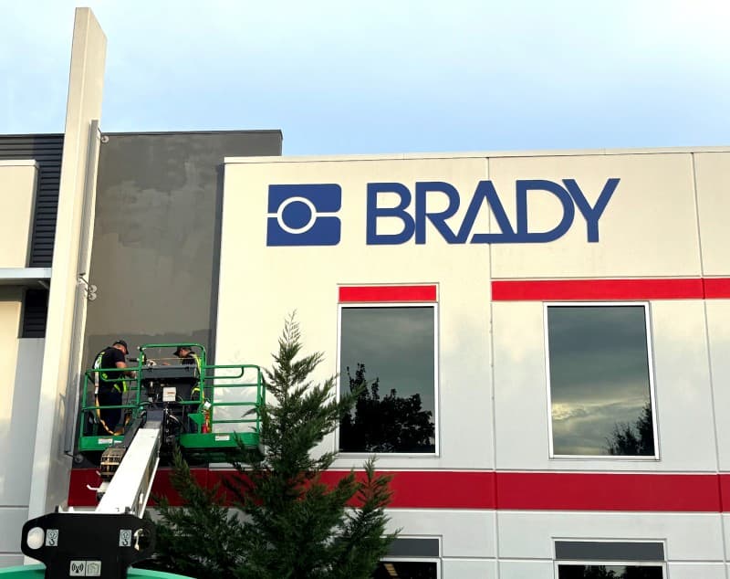 Two installers on a boom lift beside the newly fitted Brady building sign.