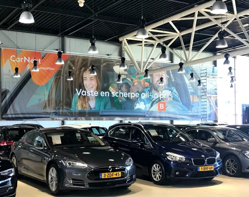 Cars on a CarNext showroom floor beneath a mural advertising a fixed, all-in price.