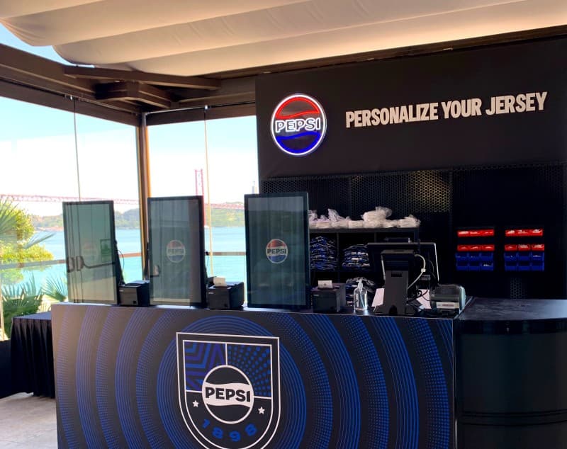 The completed Pepsi ‘Personalize your jersey’ station, kiosks and shirt racks set beneath the venue’s harbour-view windows.
