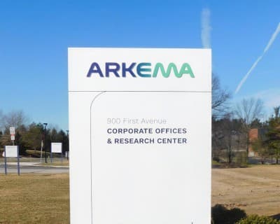 A white Arkema pylon sign on the lawn outside a corporate office and research centre.