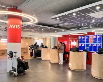 The Avis reception desks at an airport branch, staff assisting customers with luggage.