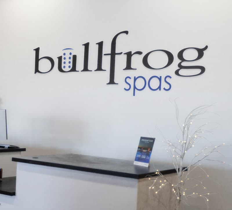 The Bullfrog Spas wordmark on a wall behind a reception desk with a lit branch display.