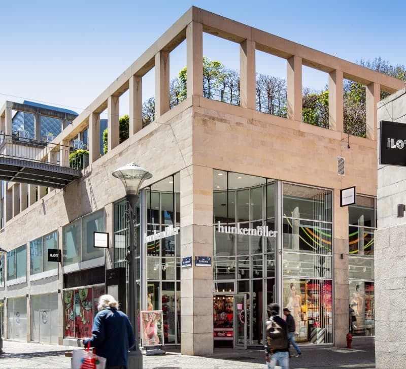 The ILOT corner building in daylight, glass storefronts including Hunkemöller beneath the colonnade.