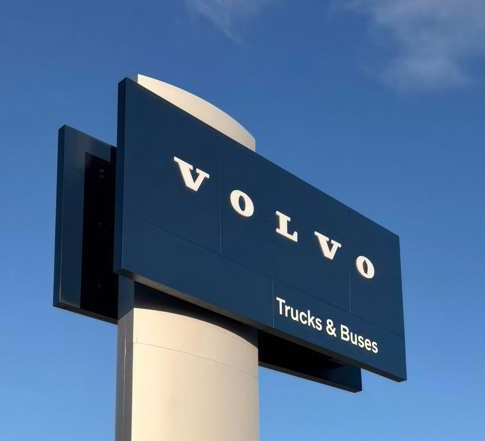 A Volvo dealership building with the wordmark on its facade, a tall roundel-branded pylon sign standing in the forecourt.