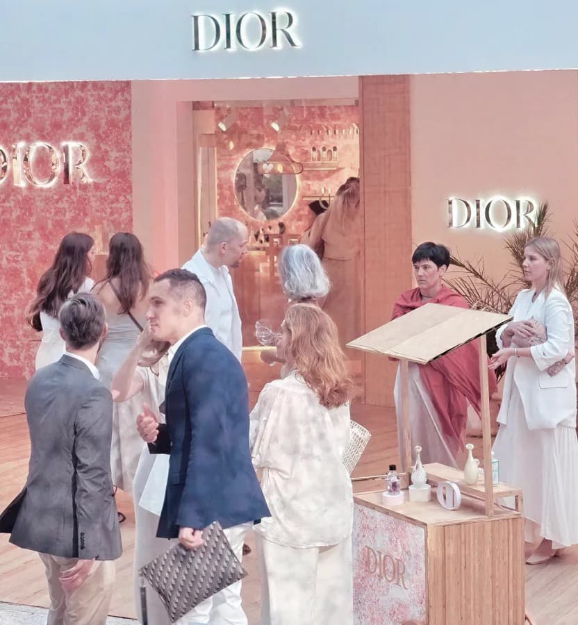 Visitors inside a Dior pop-up boutique, with backlit DIOR lettering above the entrance.