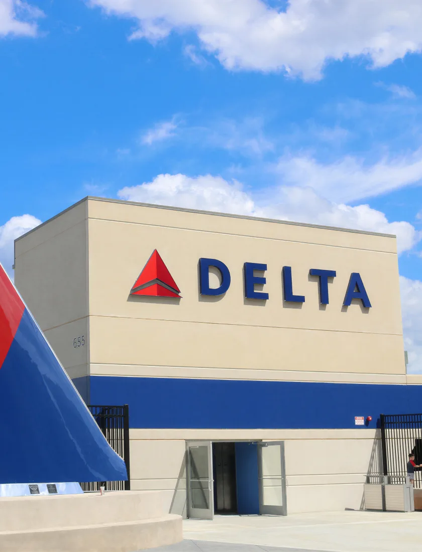 A Delta operations building with large exterior brand signage, an aircraft tail beside it