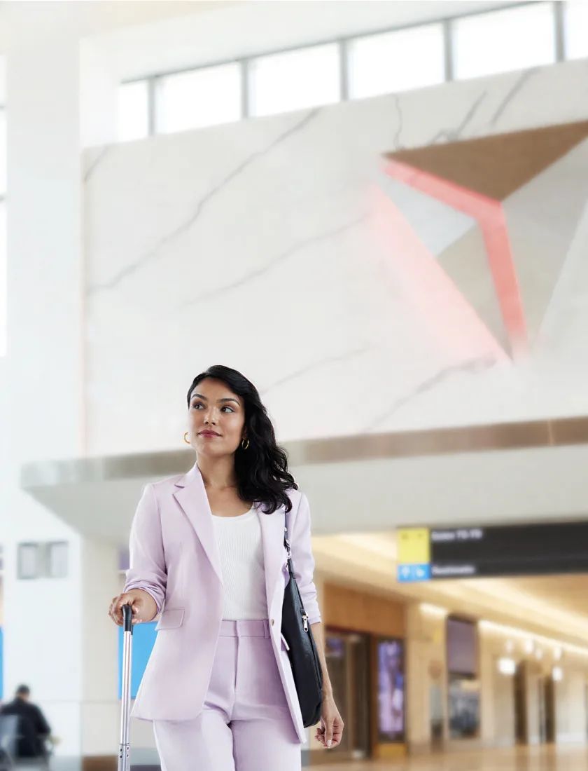 A traveller with hand luggage walking through a station concourse past overhead wayfinding signage